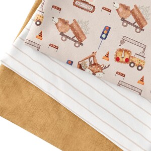 May include: Two pieces of fabric, one with a brown and white striped pattern and the other with a beige background and a repeating pattern of brown bears, deer, and construction vehicles.