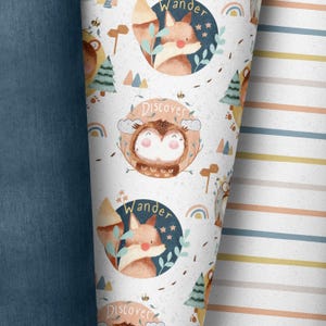 Può includere: Tessuto bianco con un motivo ripetuto di animali del bosco e le parole "Wander" e "Discover". Gli animali includono una volpe, un gufo e un orso. Il tessuto è circondato da un tessuto denim blu.