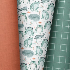 Peut inclure: Un fond blanc avec un motif répété de grenouilles vertes, de libellules et de nénuphars. Les grenouilles sont dans diverses poses, certaines sont assises, d'autres sautent et d'autres tiennent une feuille dans leur bouche. Les libellules volent autour des grenouilles et des nénuphars. Les nénuphars sont verts et ont un contour blanc.