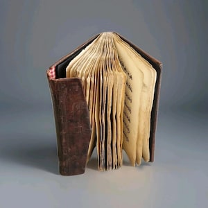 Puede incluir: Un libro antiguo abierto, con páginas amarillentas y envejecidas. El libro tiene una cubierta y lomo de cuero marrón oscuro, con desgaste visible. Las páginas están llenas de texto manuscrito, lo que sugiere un documento histórico o manuscrito.