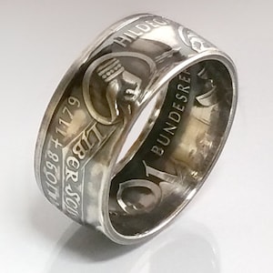 Op de afbeelding: Een zilveren ring gemaakt van een Duitse 5 Deutsche Mark-munt. De munt heeft de tekst "5 Deutsche Mark" en "Bundesrepublik Deutschland" samen met het jaar "1967".