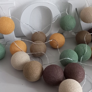 Könnte beinhalten: Eine Lichterkette aus Baumwollkugeln in verschiedenen Farben, darunter Braun, Beige, Grün und Gelb. Die Lichter sind mit einem durchsichtigen Draht verbunden und leuchten.