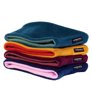 Könnte beinhalten: Ein Stapel aus fünf Fleece-Halswärmern in verschiedenen Farben, darunter Türkis, Grün, Orange, Burgunderrot und Rosa. Jeder Halswärmer hat ein kleines schwarzes Etikett mit dem Text "mydypandinus" in goldenen Buchstaben.