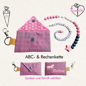 Könnte beinhalten: Ein Set Baby-Accessoires, darunter ein rosa-graues Täschchen mit floralem Muster und Druckknopfverschluss, ein Schnullerclip und ein Perlen-Alphabet-Spielzeug. Der Text "ABC- & Rechenkette" ist sichtbar.