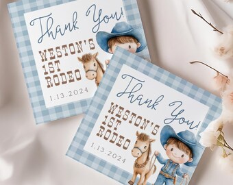 May include: Two square cards with a blue gingham border feature a watercolor illustration of a cowboy and horse. The cards read "Thank You! Weston's 1st Rodeo 1.13.2024". The cards are on a white satin surface with floral accents.