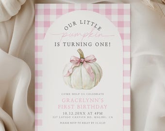 Op de afbeelding: Een uitnodiging voor de eerste verjaardag met een roze ruitpatroon en de tekst "Our Little Pumpkin is Turning One!". Een aquarel pompoen met een roze strik is afgebeeld. Witte pompoenen en een brandende kaars staan op de achtergrond.