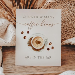May include: A decorative card with the text "Guess how many coffee beans are in the jar." The card features a coffee cup with a heart design and scattered coffee beans. The card is on a wooden board with a neutral-toned background.
