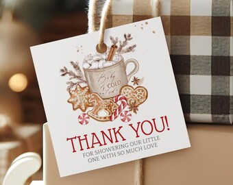 Op de afbeelding: Een feestelijke vakantiescène met ingepakte cadeaus op een miniatuur witte slee. Eén cadeau is verpakt in bruin en wit geruit papier, de andere is effen bruin. Een label met "THANK YOU!" en een cacao-illustratie hangt eraan.