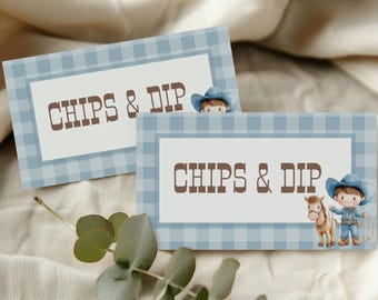 Könnte beinhalten: Zwei blau karierte Karten mit dem Text "CHIPS & DIP" in Braun. Eine Karte zeigt eine Cowboy-Illustration. Die Karten liegen auf einer beigefarbenen Stoffoberfläche, mit grünen Blättern im Vordergrund.