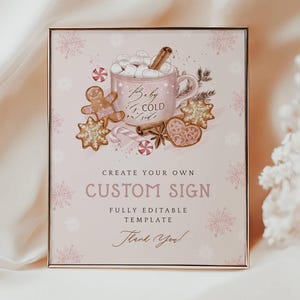 May include: A framed custom sign with a pink background and gold frame. The sign features a watercolour illustration of a mug of hot chocolate, gingerbread biscuits, and candy canes. Text includes "Baby It's Cold Outside" and "Create Your Own Custom Sign."