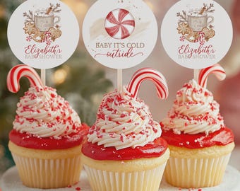 May include: Three cupcakes with white frosting, red sprinkles, and candy cane decorations. Each cupcake has a round topper with a holiday design and text that reads "Baby it's cold outside" and "Elizabeth's Baby Shower".