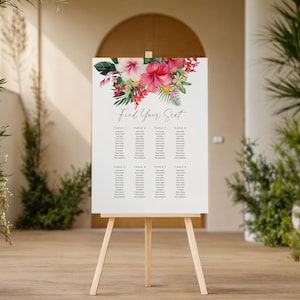 May include: A white sign on a wooden easel with the text "Find Your Seat". The sign is decorated with a floral arrangement of pink, red, and green flowers. The sign lists names under table numbers.
