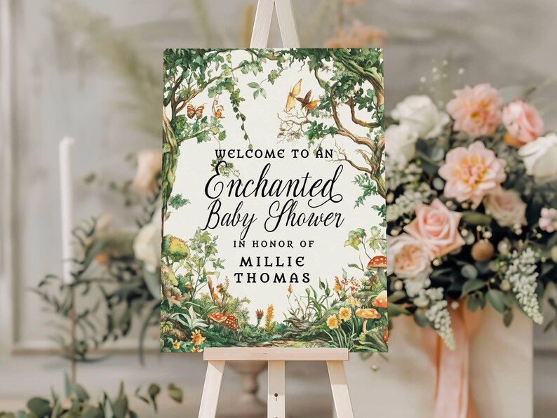 May include: A rectangular sign featuring a forest illustration with trees, vines, butterflies, and mushrooms. The text reads: Welcome to an Enchanted Baby Shower in honor of Millie Thomas. The sign is displayed on a light-colored wooden easel.