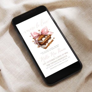Könnte beinhalten: Ein Smartphone zeigt eine Babyparty-Einladung. Die Einladung zeigt eine Aquarellillustration eines S'more mit einer rosa Schleife. Der Text enthält "smore to love" und Details für die Babyparty von Millie Mae Thomas.