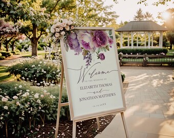 May include: A wedding welcome sign with a purple and white floral design. The sign reads "Welcome to the wedding of Elizabeth Thomas and Jonathan Matthews 12.12.20XX".