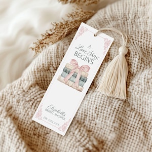 May include: A white bookmark with a pink tassel. The bookmark features a stack of books tied with a pink ribbon and the text "A Love Story Begins". Below the books, the text reads "Elizabeth's Bridal Shower Jan. 13th 20XX".