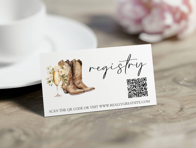 K&ouml;nnte beinhalten: Wei&szlig;e Karte mit dem Wort &bdquo;registry&ldquo; in Schreibschrift. Die Karte zeigt eine Aquarellillustration von braunen Cowboy-Stiefeln, einem Sektglas und Blumen. Ein QR-Code und eine Website-Adresse sind ebenfalls enthalten.