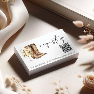 K&ouml;nnte beinhalten: Eine wei&szlig;e Registrierungskarte mit Illustrationen von Cowboy-Stiefeln, Champagner und Blumen. Das Wort "registry" ist in Schrift geschrieben, mit einem QR-Code und einer Website-Adresse darunter.