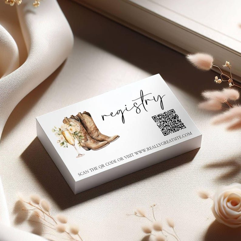 K&ouml;nnte beinhalten: Eine wei&szlig;e Registrierungskarte mit Illustrationen von Cowboy-Stiefeln, Champagner und Blumen. Das Wort "registry" ist in Schrift geschrieben, mit einem QR-Code und einer Website-Adresse darunter.