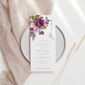 Puede incluir: Una tarjeta de menú de boda con un diseño floral con flores moradas y blancas. El menú incluye opciones de entrantes, platos principales y postres. El texto en la tarjeta dice "The Menu", "Starters", "Main", "Alternate Serving", "Dessert", "Carrot Cake", "Elizabeth & Jonathan".
