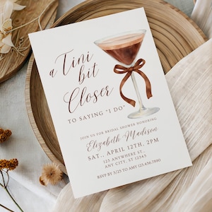 Puede incluir: Una tarjeta de invitación rectangular para despedida de soltera con una ilustración en acuarela de una copa de martini con un lazo marrón atado al tallo. El texto dice: a Tini bit Closer TO SAYING I DO, JOIN US FOR BRIDAL SHOWER HONORING Elizabeth Madison.