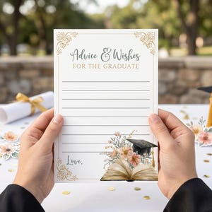 May include: A white rectangular graduation advice and wishes card featuring gold decorative corners, black lined text areas, and a printed illustration of an open book, pink flowers, and a black graduation cap with a gold tassel at the bottom.