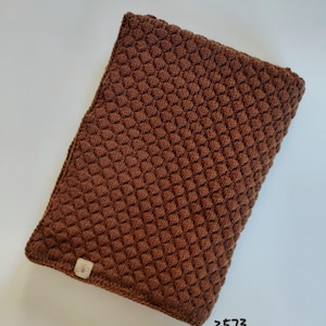 May include: A rectangular brown knitted cover featuring a textured honeycomb stitch pattern. A small rectangular fabric tag with a bee icon is attached to the bottom left corner. The text 2573 helles braun is printed in black near the bottom right.