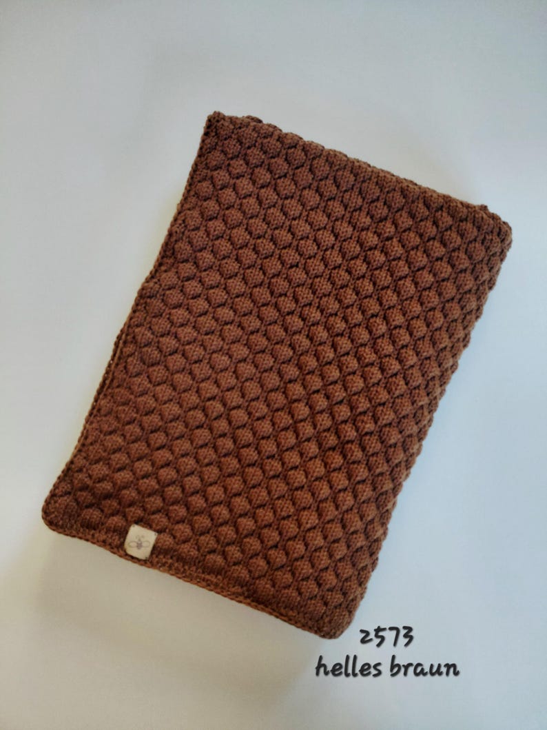 May include: A rectangular brown knitted cover featuring a textured honeycomb stitch pattern. A small rectangular fabric tag with a bee icon is attached to the bottom left corner. The text 2573 helles braun is printed in black near the bottom right.