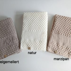 May include: Three rectangular knitted blankets in beige, white, and light tan. Each blanket features a textured diamond pattern, a smooth central band, and a small square tag at the bottom. The text beigemeliert, natur, and marzipan is visible.