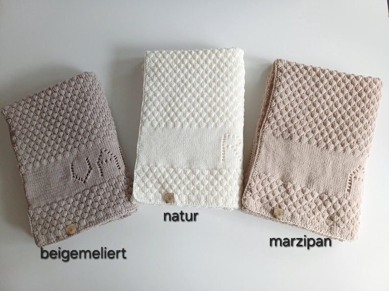 May include: Three rectangular knitted blankets in beige, white, and light tan. Each blanket features a textured diamond pattern, a smooth central band, and a small square tag at the bottom. The text beigemeliert, natur, and marzipan is visible.