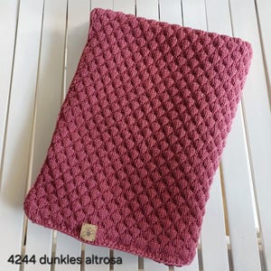 May include: A rectangular knitted blanket in a deep dusty rose color featuring a textured diamond pattern. A small square tan leather tag with a bee icon is attached to the bottom left corner. The text 4244 dunkles altrosa is visible.