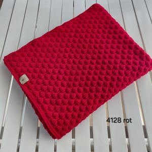 May include: A vibrant red crocheted blanket featuring a textured bobble stitch pattern throughout. A small rectangular wooden tag with a bee icon is attached to the corner. The text 4128 rot is printed in the lower right corner of the image.