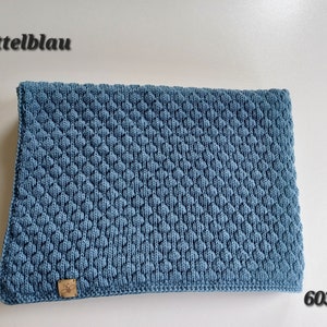 May include: A rectangular medium blue knitted blanket featuring a textured honeycomb pattern. The fabric has a small tan leather tag with a bee icon in the bottom left corner. The text "mittelblau" and "6033" are visible in the corners.