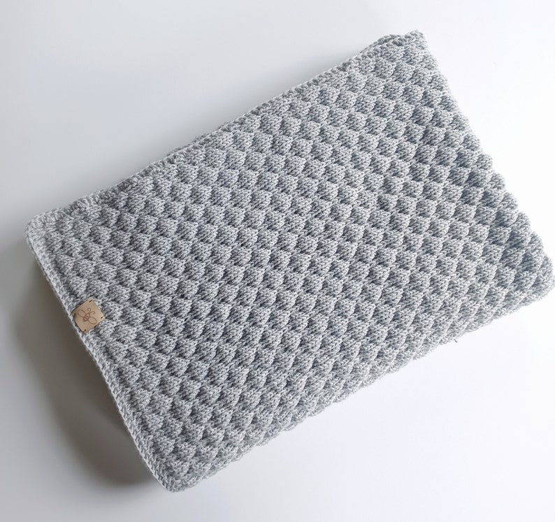 以下が含まれることがあります： グレーのダイヤモンド模様の編み地のベビーブランケット