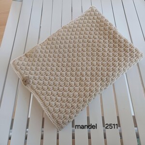 May include: A rectangular beige knitted blanket featuring a consistent textured bobble stitch pattern throughout. A small brown rectangular tag with a black logo is attached to the side. The text mandel 2511 is printed in black on the surface.