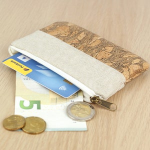 Puede incluir: Una peque&ntilde;a bolsa con cremallera de corcho y tela con un tirador de cremallera blanco. La bolsa est&aacute; abierta y contiene una tarjeta de cr&eacute;dito azul, un billete de cinco euros y dos monedas de oro.