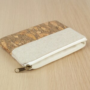 Puede incluir: Una peque&ntilde;a bolsa con cremallera hecha de corcho y tela. La bolsa es beige y marr&oacute;n con una cremallera blanca.