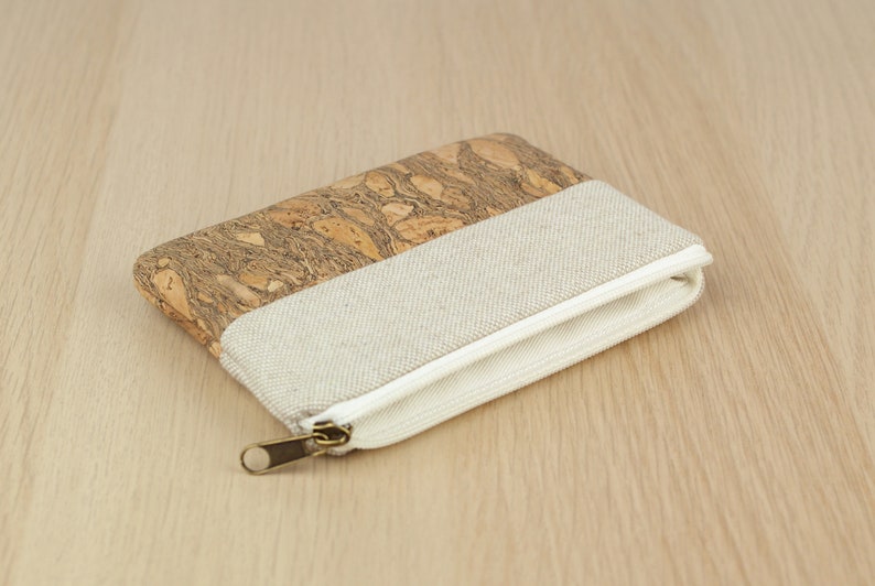Puede incluir: Una peque&ntilde;a bolsa con cremallera hecha de corcho y tela. La bolsa es beige y marr&oacute;n con una cremallera blanca.