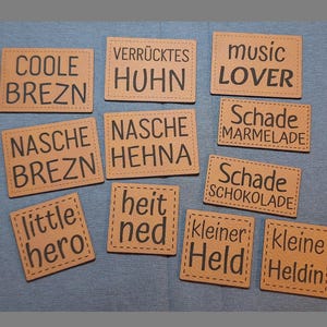 May include: A collection of tan rectangular patches with black text. Phrases include "COOLE BREZN", "music LOVER", "little hero", and others. The patches are stitched around the edges and are arranged on a blue surface.