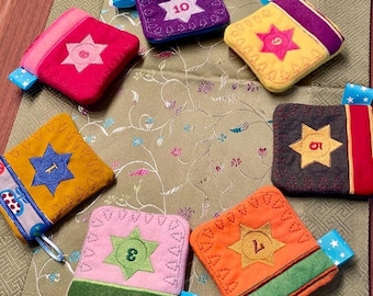May include: Set of ten felt pouches with star-shaped patches and numbers 1 through 10 embroidered on them. The pouches are in various colours, including pink, purple, yellow, orange, and brown.