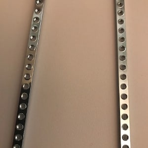 May include: Two silver metal strips with evenly spaced round holes.