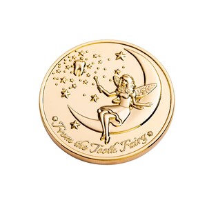 May include: A gold-colored coin with a fairy sitting on a crescent moon. The fairy is holding a wand and there are stars in the background. The coin says "From the Tooth Fairy".