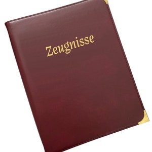 Könnte beinhalten: Ein bordeauxroter Lederordner mit goldenen Ecken und dem in goldenen Lettern geprägten Wort "Zeugnisse".