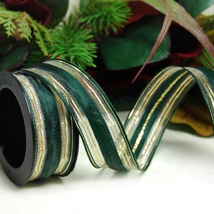 Pode incluir: Um carretel de fita verde e dourada com acabamento acetinado. A fita tem um padrão de chevron e está enrolada em torno de um carretel preto.