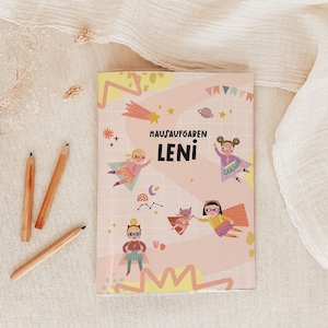 Può includere: Un quaderno rosa con la scritta "HAUSAUFGABEN LENI" e illustrazioni di supereroi dei cartoni animati. Matite di legno sono posizionate vicino al quaderno, che si trova su un tessuto beige. La copertina presenta stelle, una stella cadente e altri elementi decorativi.