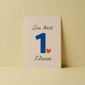 Könnte beinhalten: Eine rechteckige Karte mit den Worten "Du bist 1. Klasse" in schwarzer Schrift. Die Zahl 1 ist blau, und ein kleines rotes Herz ist darunter. Der Hintergrund hat ein hellgelbes Gittermuster.