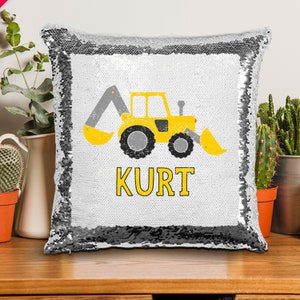 May include: A white and silver reversible sequin pillow with a yellow excavator and the name "KURT" printed on it.
