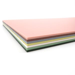May include: A stack of rectangular, multi-colored sheets. The top sheet is a light pink, followed by layers of brown, gray, yellow, white, and green. The sheets are stacked neatly, with a white background.