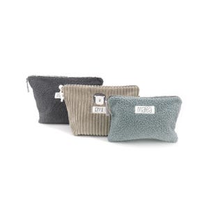 May include: Three small, textured pouches in gray, tan, and blue-green. The gray pouch has a zipper and the name "Pa" on a tag. The tan pouch has vertical ribbing, a lion applique, and the name "Emi". The blue-green pouch has the name "Malea".
