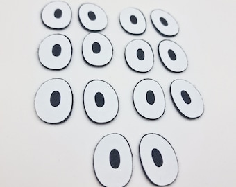 May include: A set of 14 white googly eyes with black pupils. The eyes are arranged in a staggered pattern on a white background.